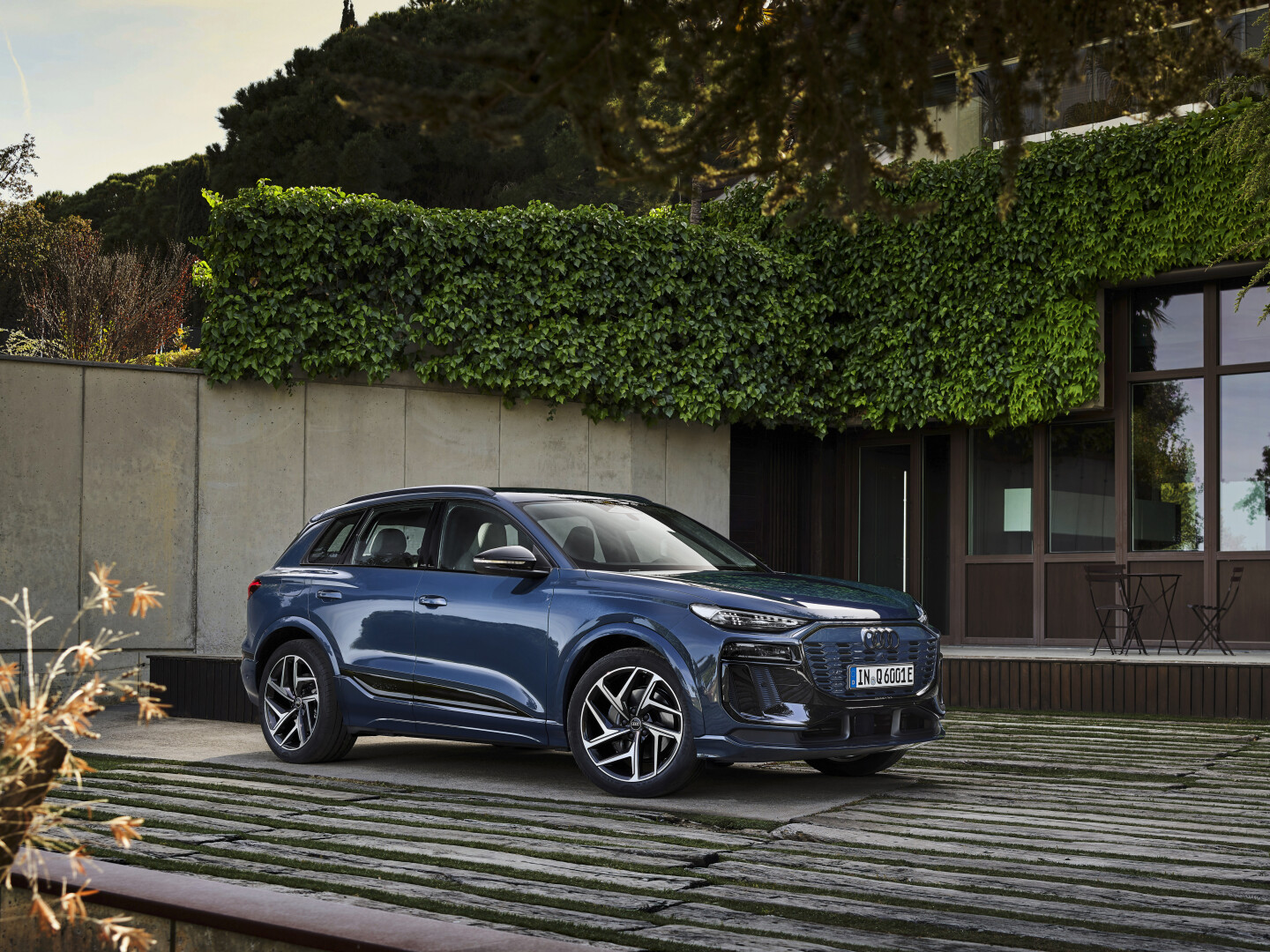 Metalic blue Audi Q6 e-tron, parked next to a eco friendly home shrouded in ivy vines