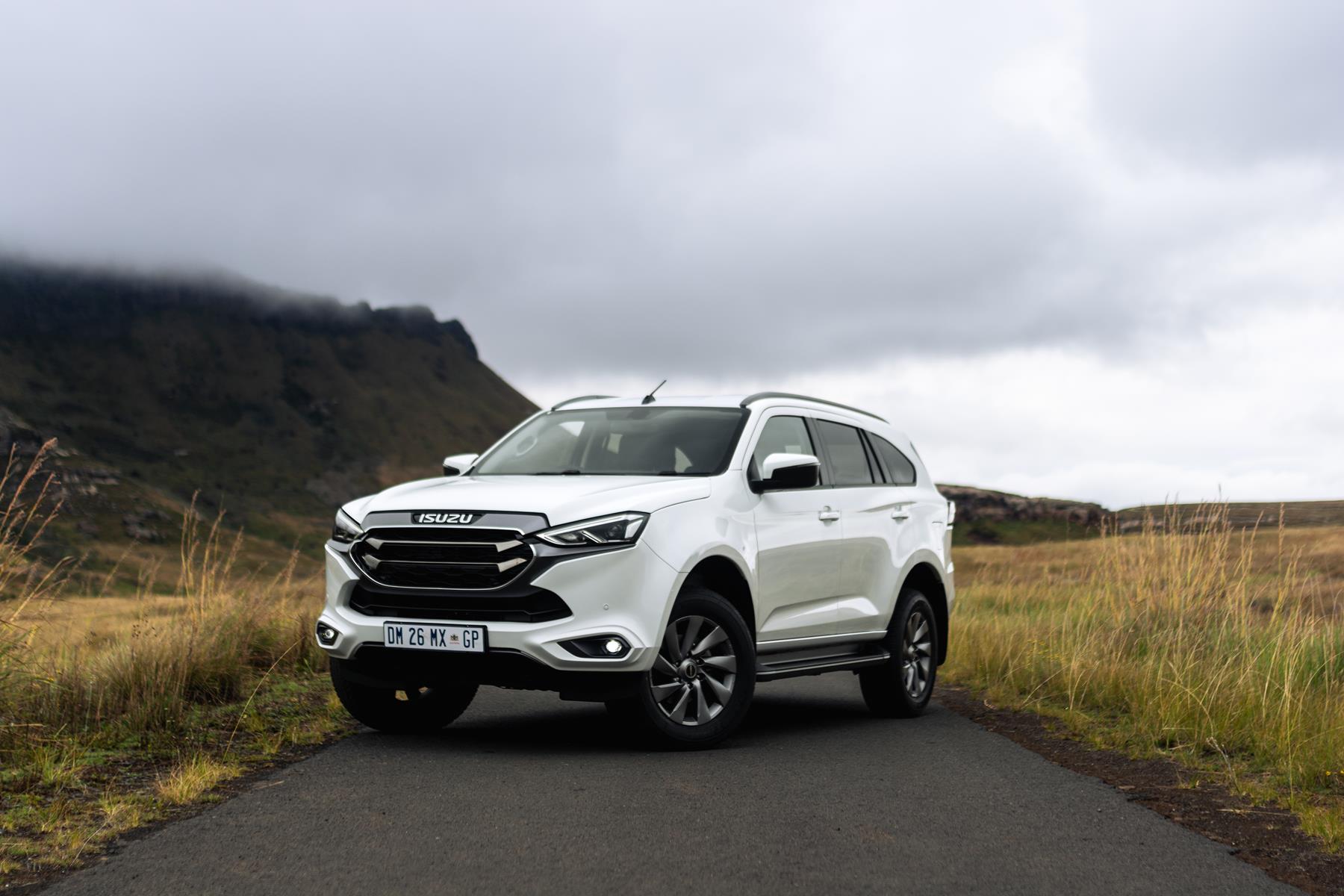 A white Izuzu D-Max on a tar road with long grass