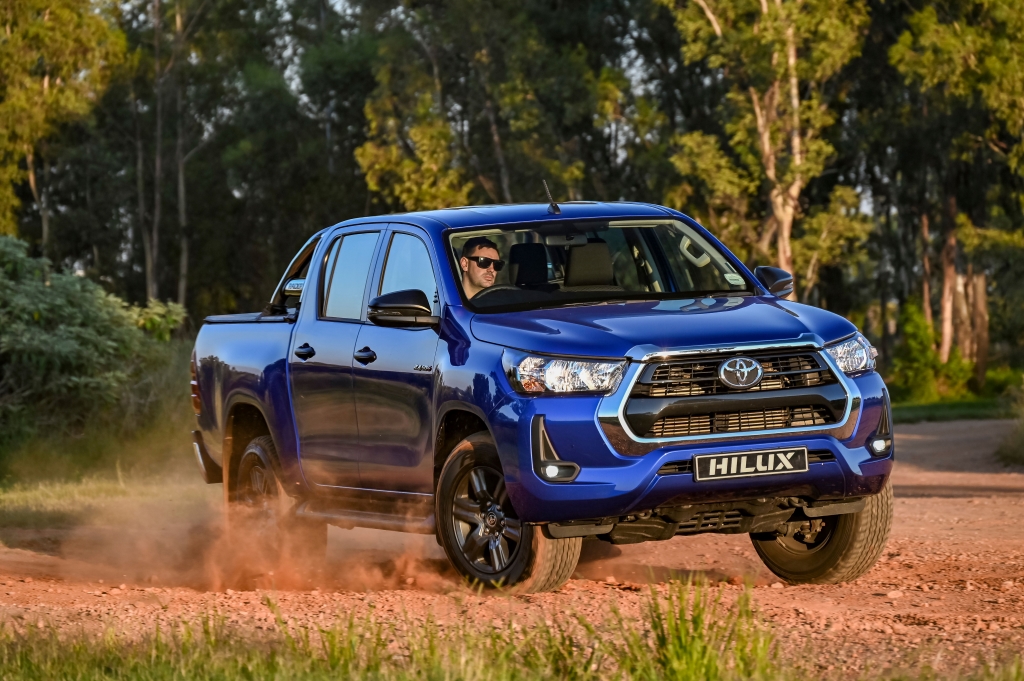 Blue Toyota Hilux driving on a dirt road with tress in the background