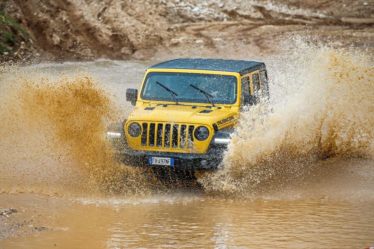 A yellow Jeep driving through the mud fast