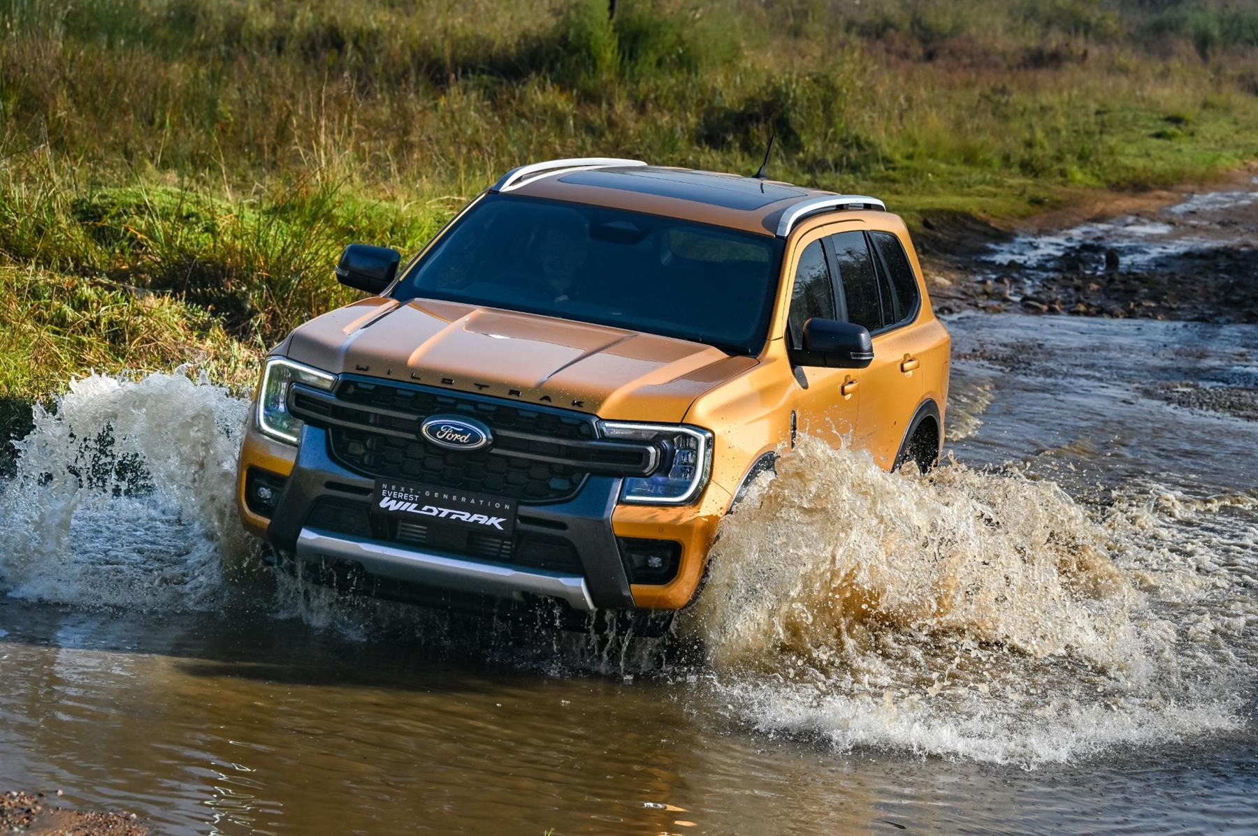 Orange Ford Everest Wildtrack racing through a stream of water