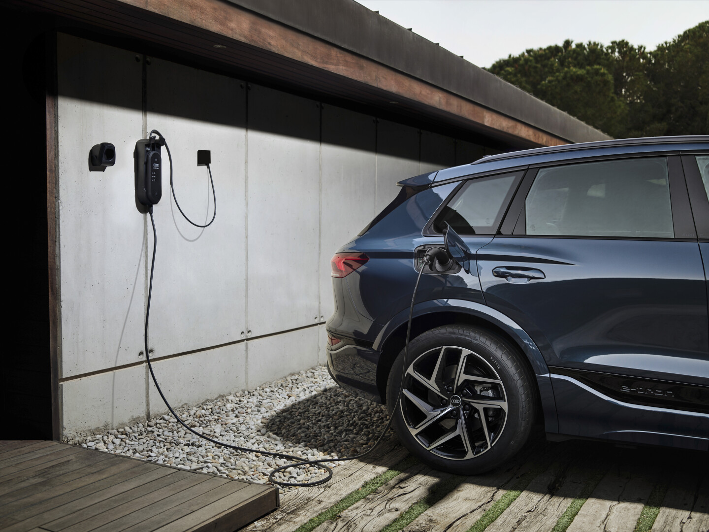 A metallic blue Audi Q6 e-tron backed up to a chanrging point on eco friendly house